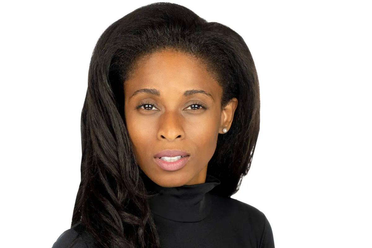 Headshot of a woman with long dark hair and a pearl earring, serious expression, in a black turtleneck, on a white background