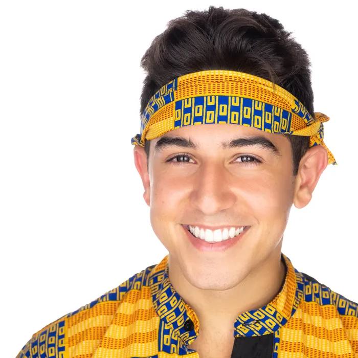 Headshot of a young man in a yellow and blue patterned headband and matching shirt, smiling widely, on a white background